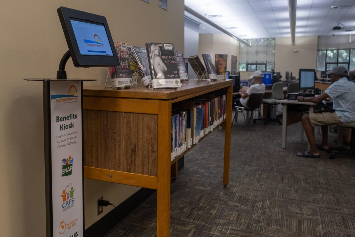 Self-service tablet kiosk on a floor stand beside a library shelf