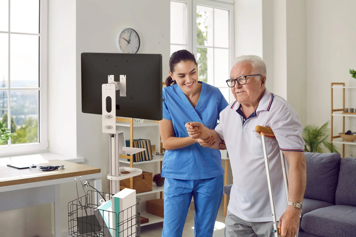 Nurse helping a patient beside a rolling medical cart with a monitor