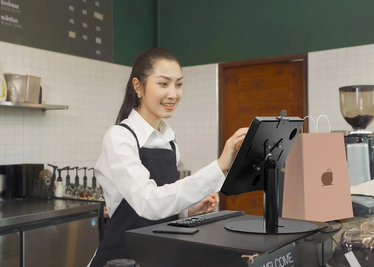 Café worker using an iPad in a black locking kiosk stand at the counter