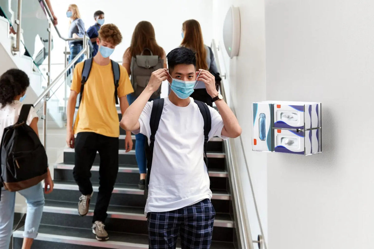 Students on a campus staircase beside a wall-mounted sanitizing kit box