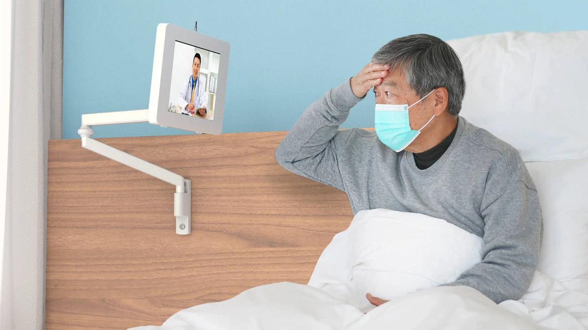 Patient in bed on a video call with a tablet on a medical arm wall mount